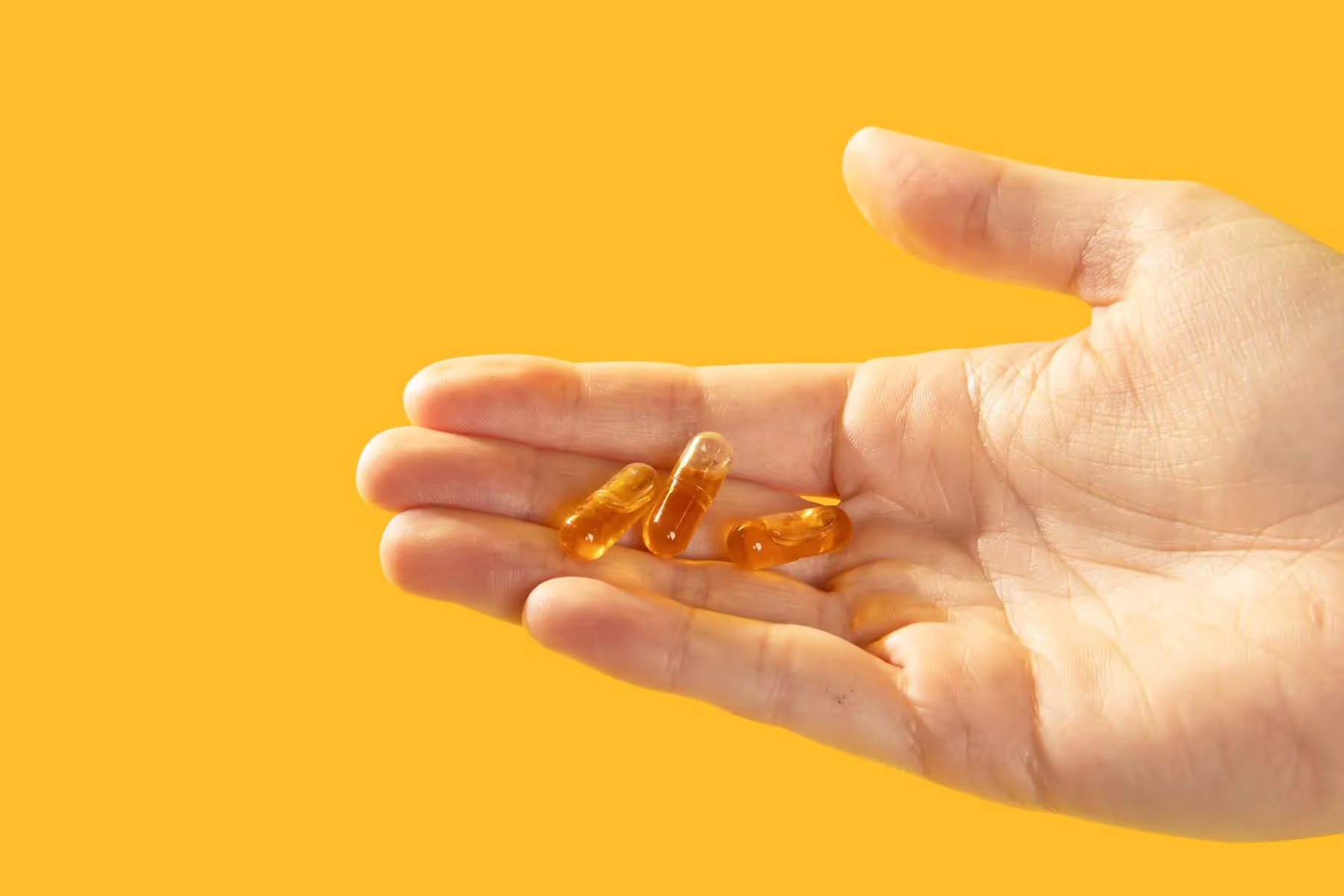 a hand model holding capsules on a yellow backdrop